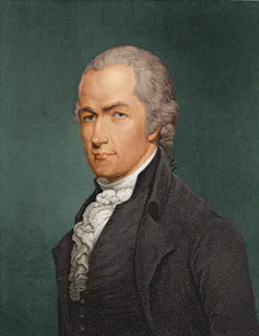 A gray-haired man dressed in a Colonial manner, with a ruffled white shirt and gray waistcoat and jacket.