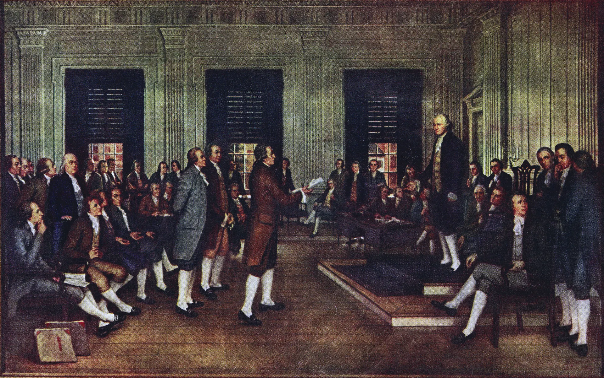 A large, formal hall with many men in Colonial dress talking, some from a stage.