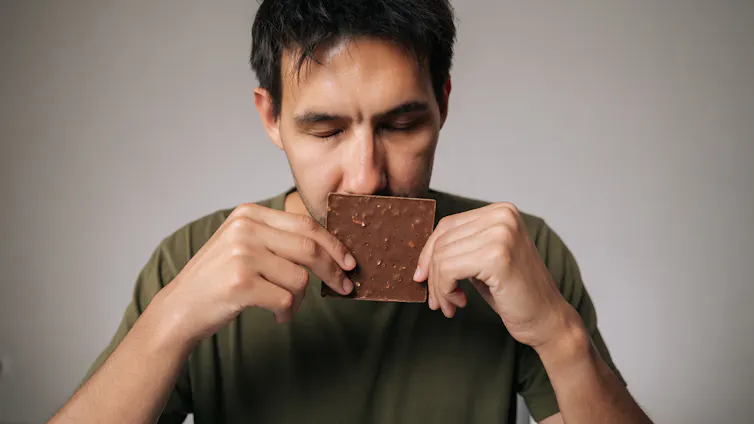 Man, eyes shut, sniffing chocolate bar.