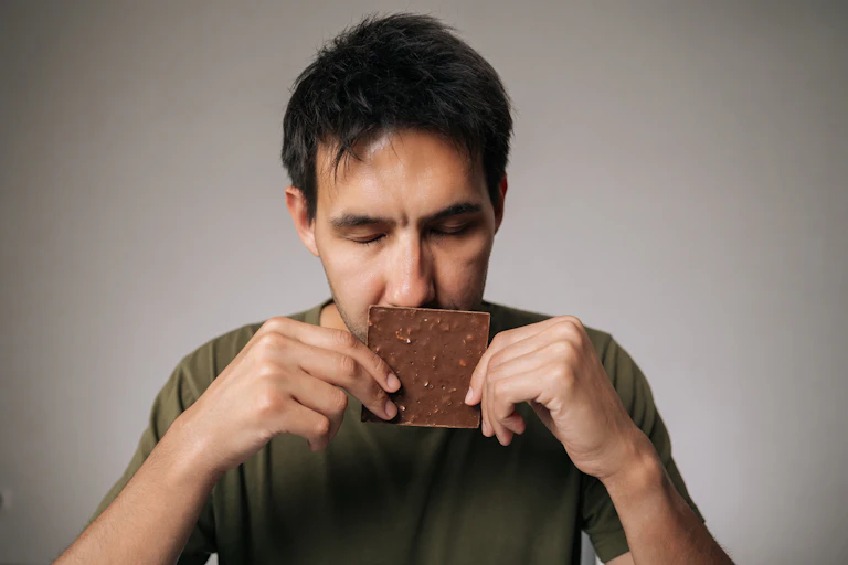 Man, eyes shut, sniffing chocolate bar.