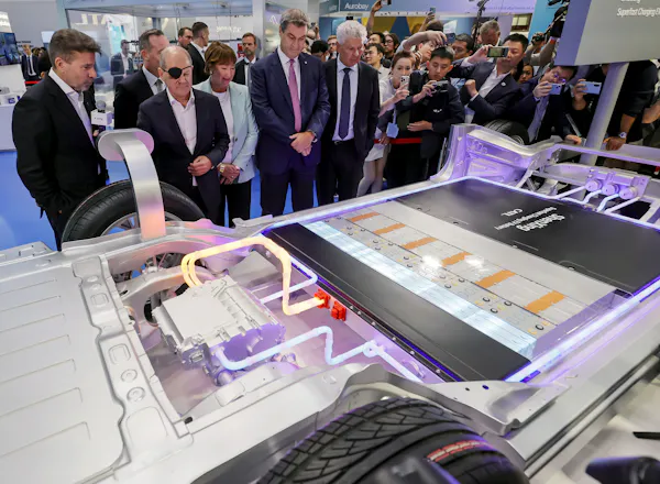 a group of men looking at the battery pack of an electric vehicle at a car show.
