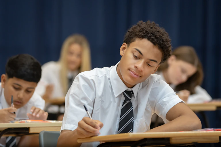 Confident high school student sitting an exam in a large hall.