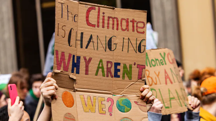 homemade cardboard protest sign, coloured letters spell: The climate is changing, why aren't we