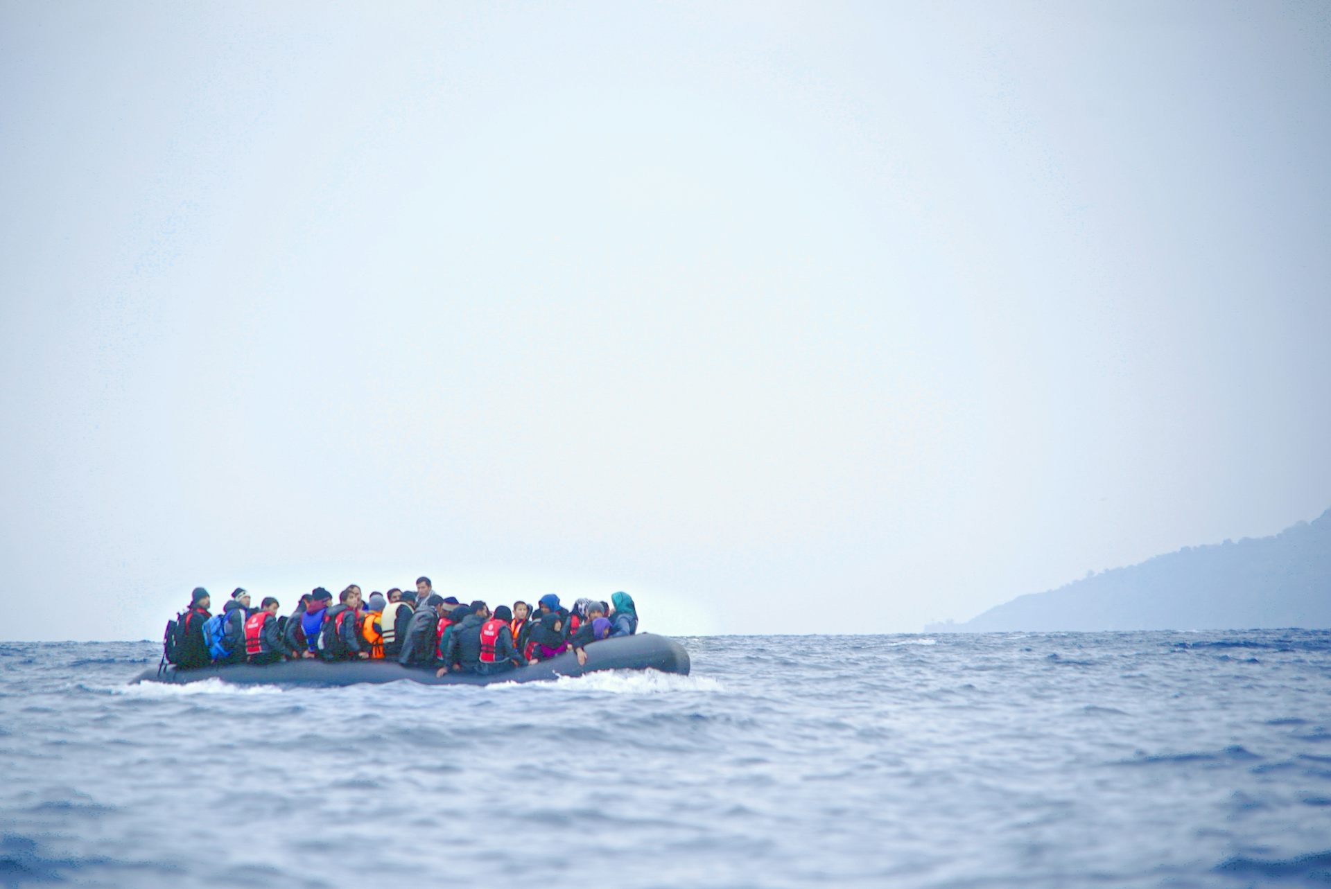 A colour photograph of people on an inflatable dinghy on a grey sea with a sliver of land in the background.