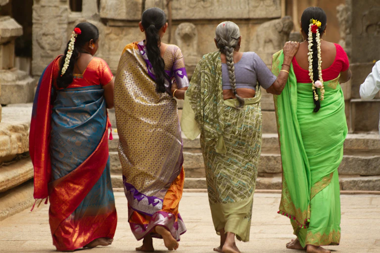 Cuatro mujeres indias con sari tradicional caminando junto a los antiguos pilares de piedra tallada de un templo.
