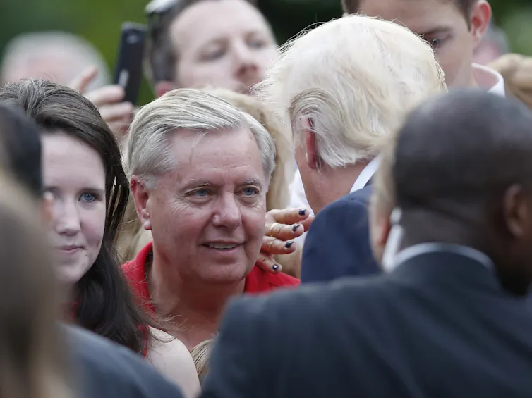 Cómo la aguda capacidad de Lindsey Graham para leer el momento lo impulsó a la relevancia política durante tres décadas 1 Un hombre con camisa roja mira a otro hombre con traje y corbata.