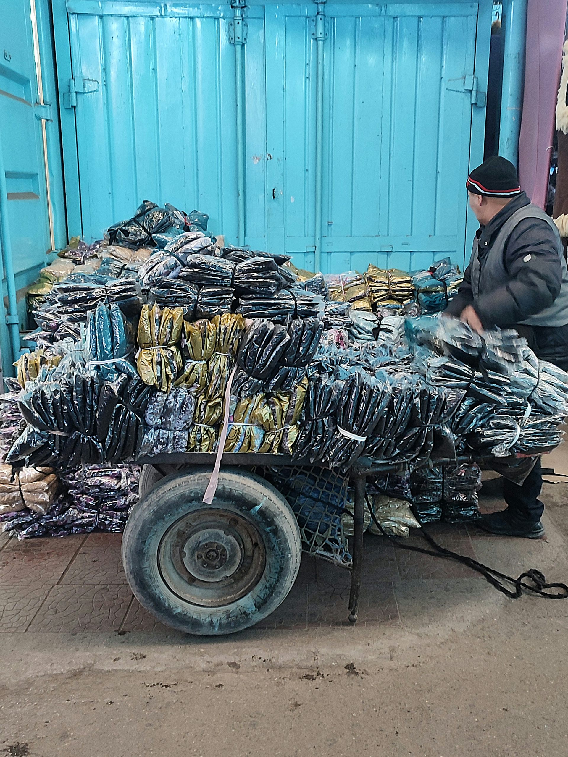 A man with a cart piled high with plastic-wrapped clothing