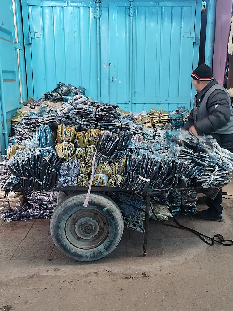 A man with a cart piled high with plastic-wrapped clothing