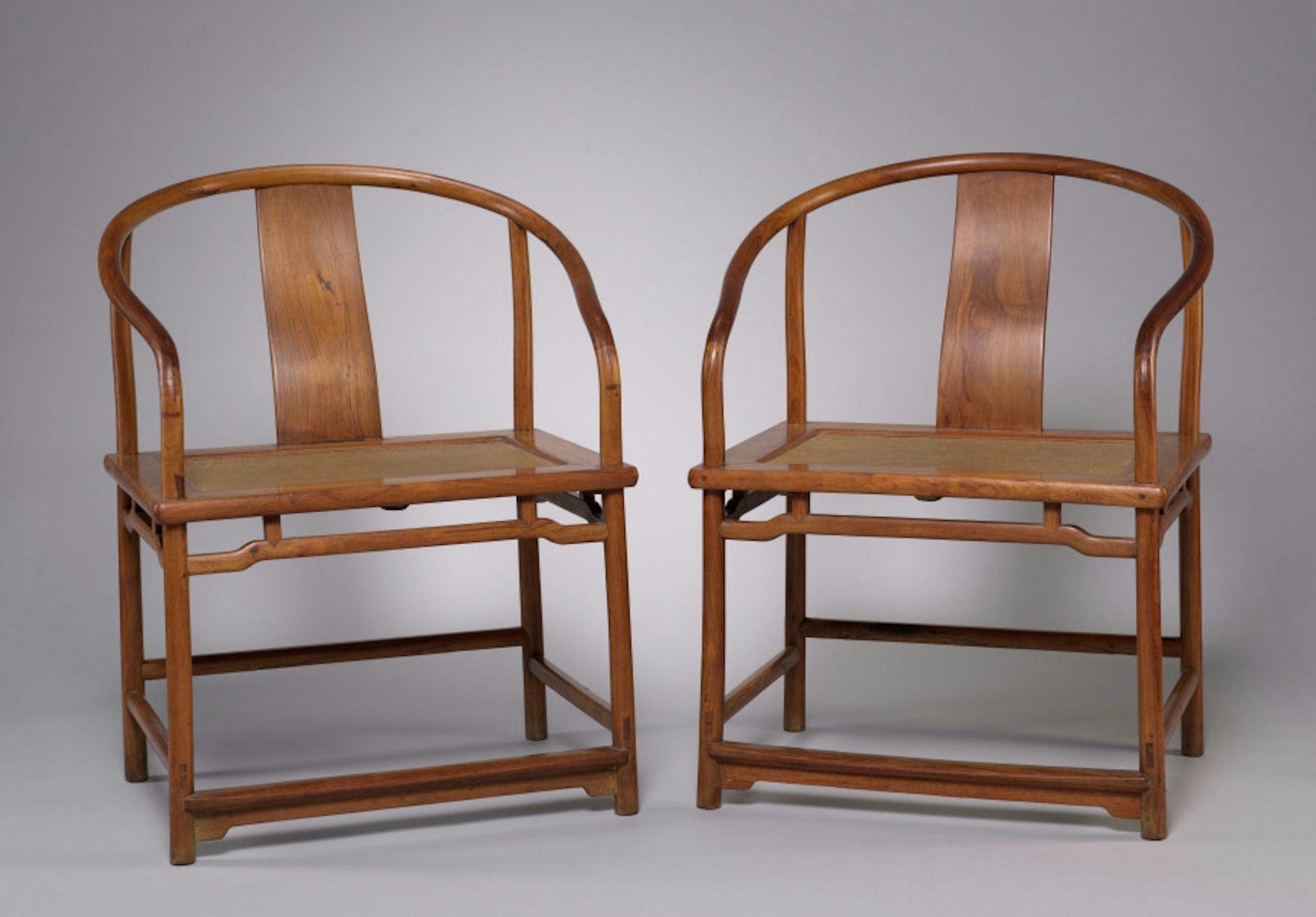 Two wooden chairs shine in gallery light.