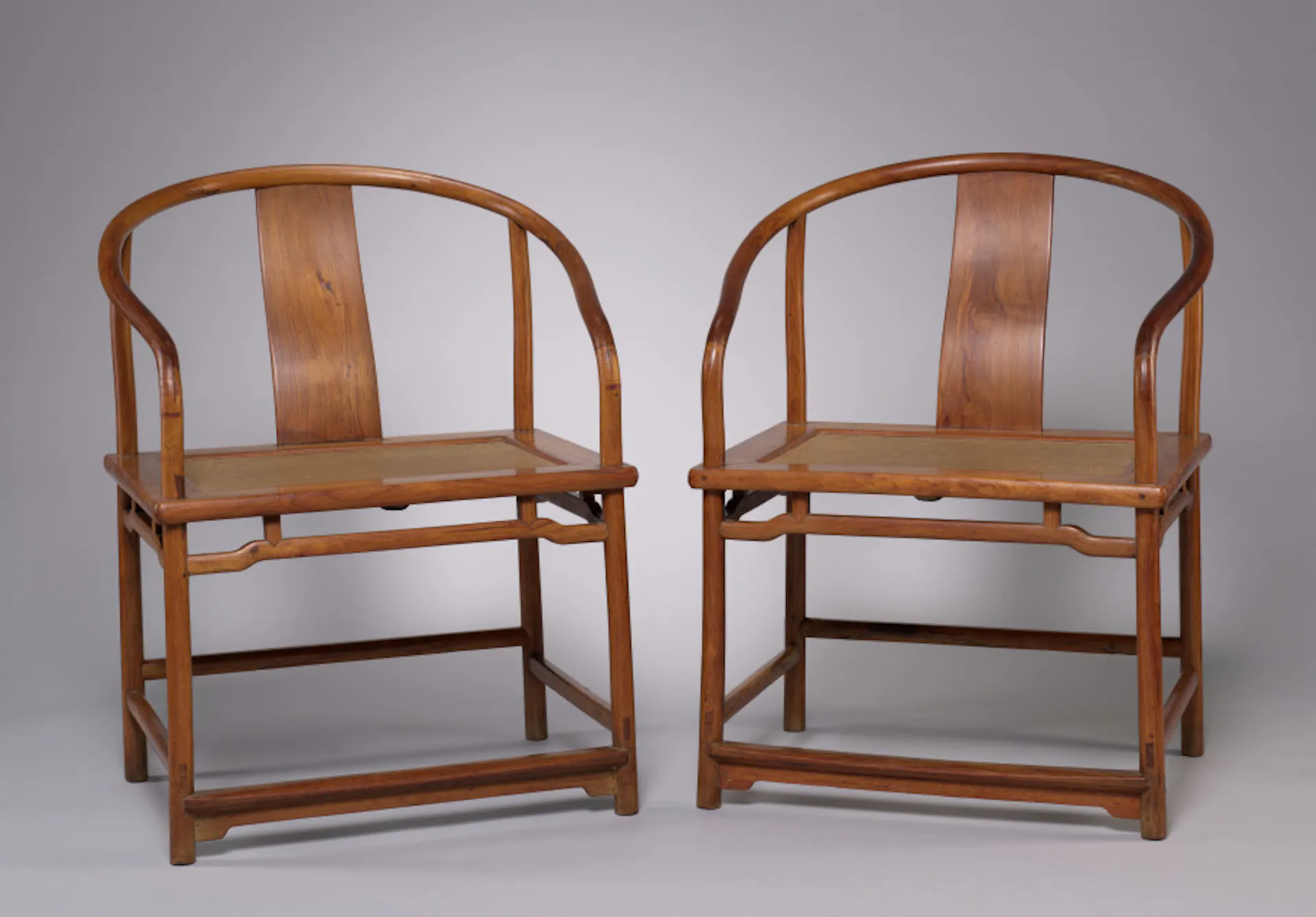 Two wooden chairs shine in gallery light.