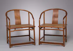 Two wooden chairs shine in gallery light.
