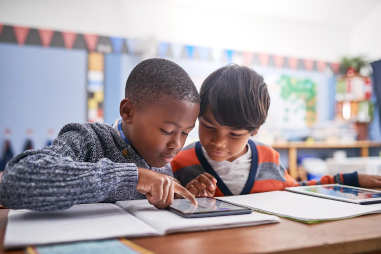 two youg boys in a classroom look at a tablet screen