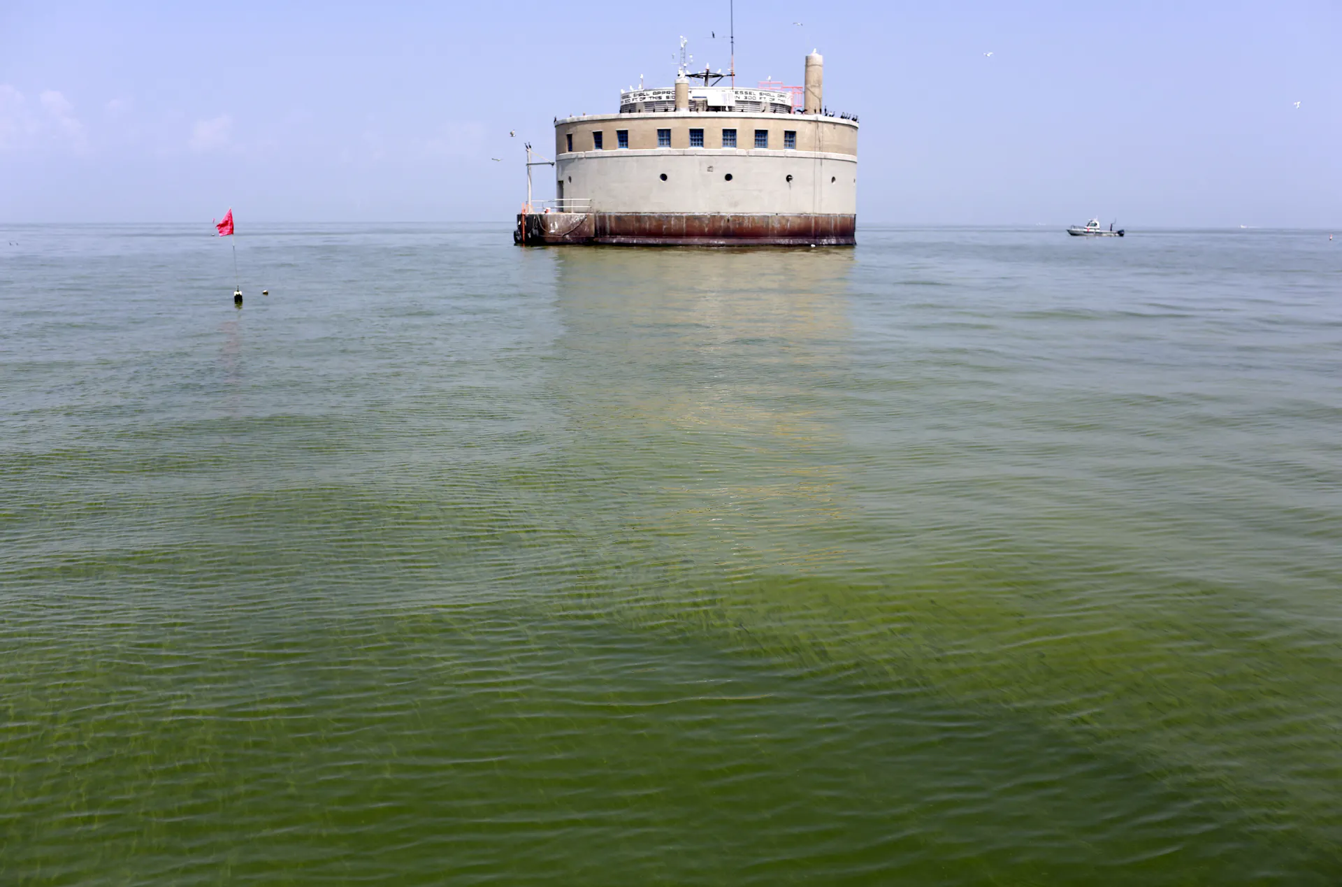 A large round building emerges from the surface of a body of water covered in green algae.