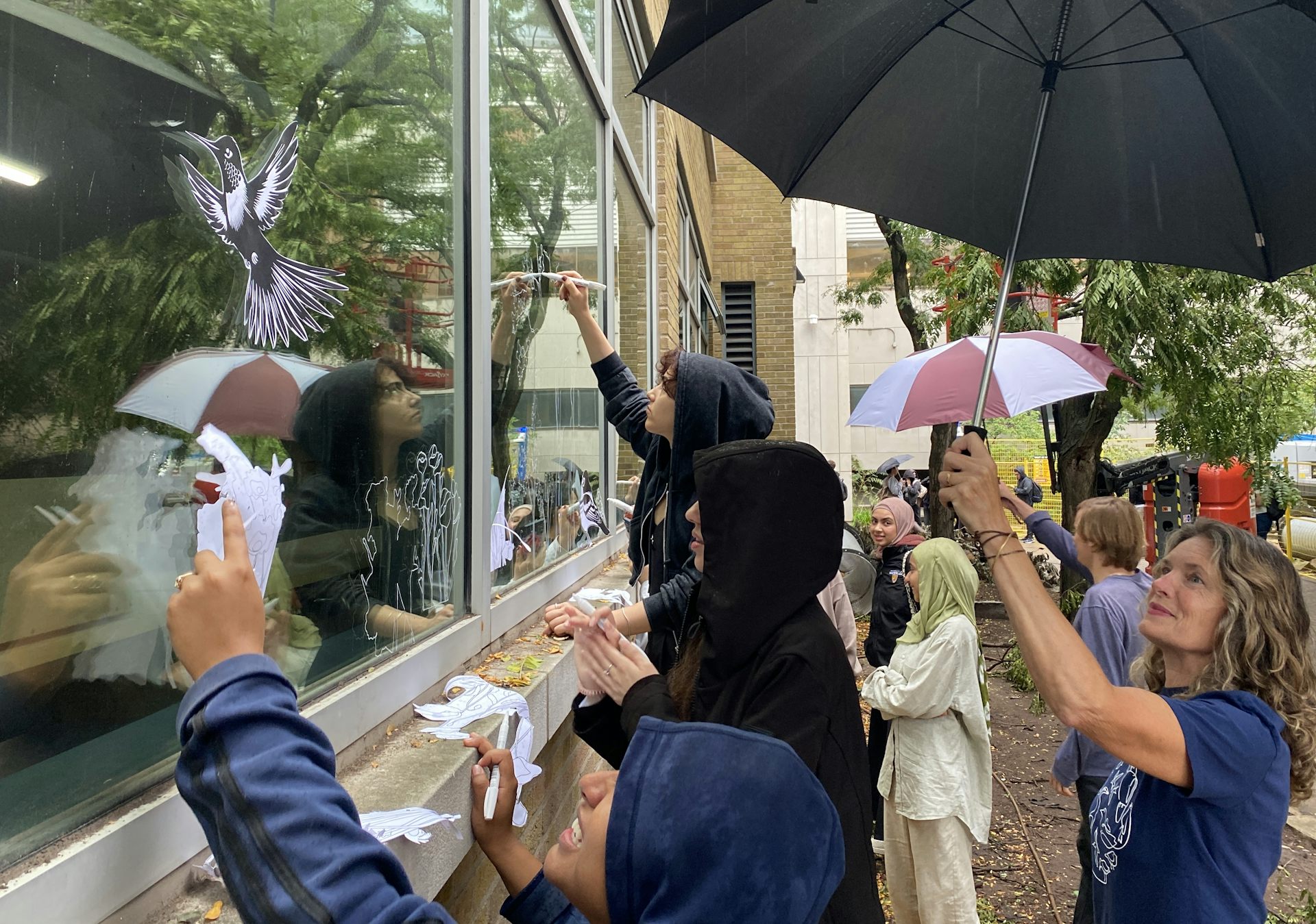A group of students draws a design with birds on a set of windows.