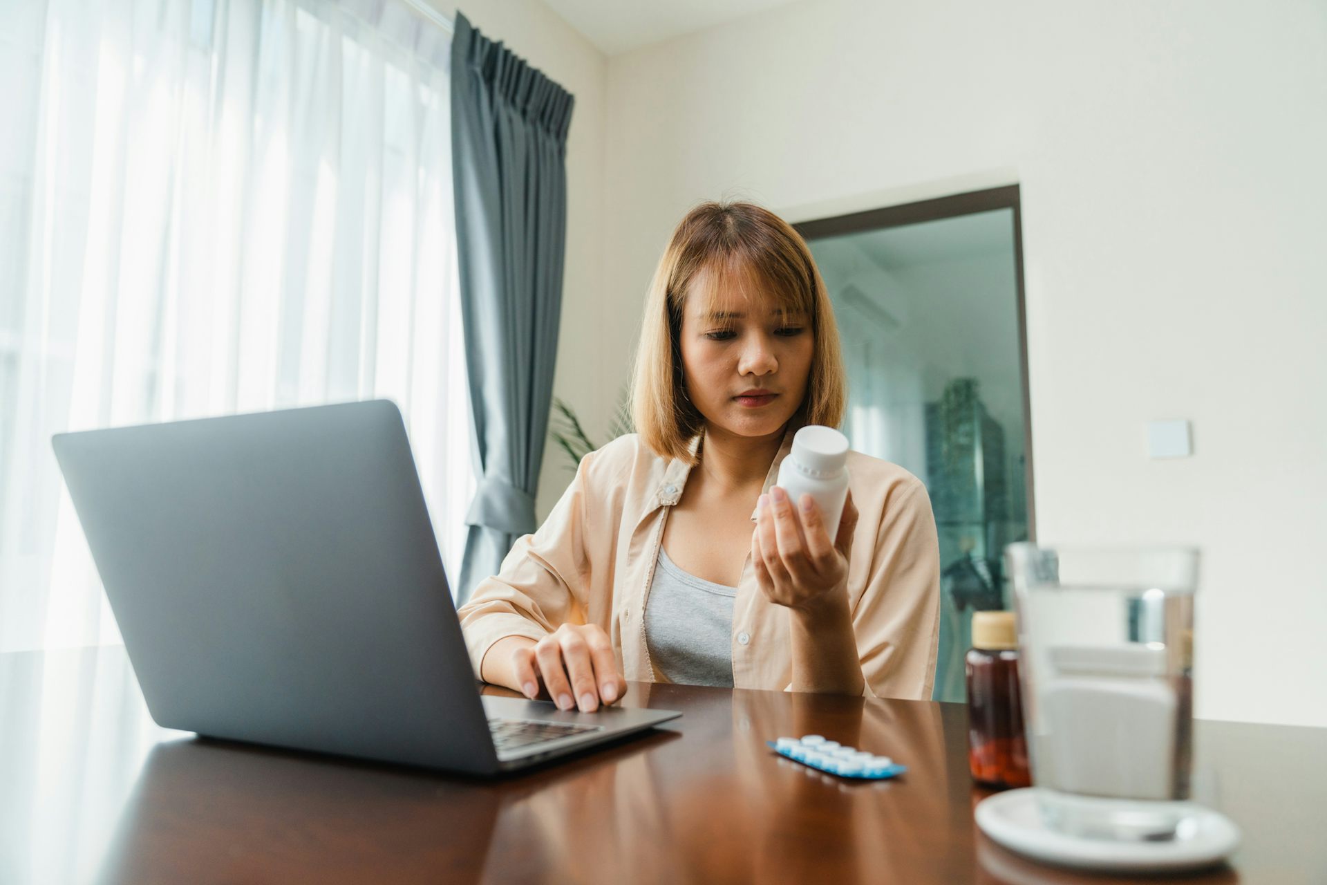 Young woman hold medicine searching information online by laptop in living room at home.