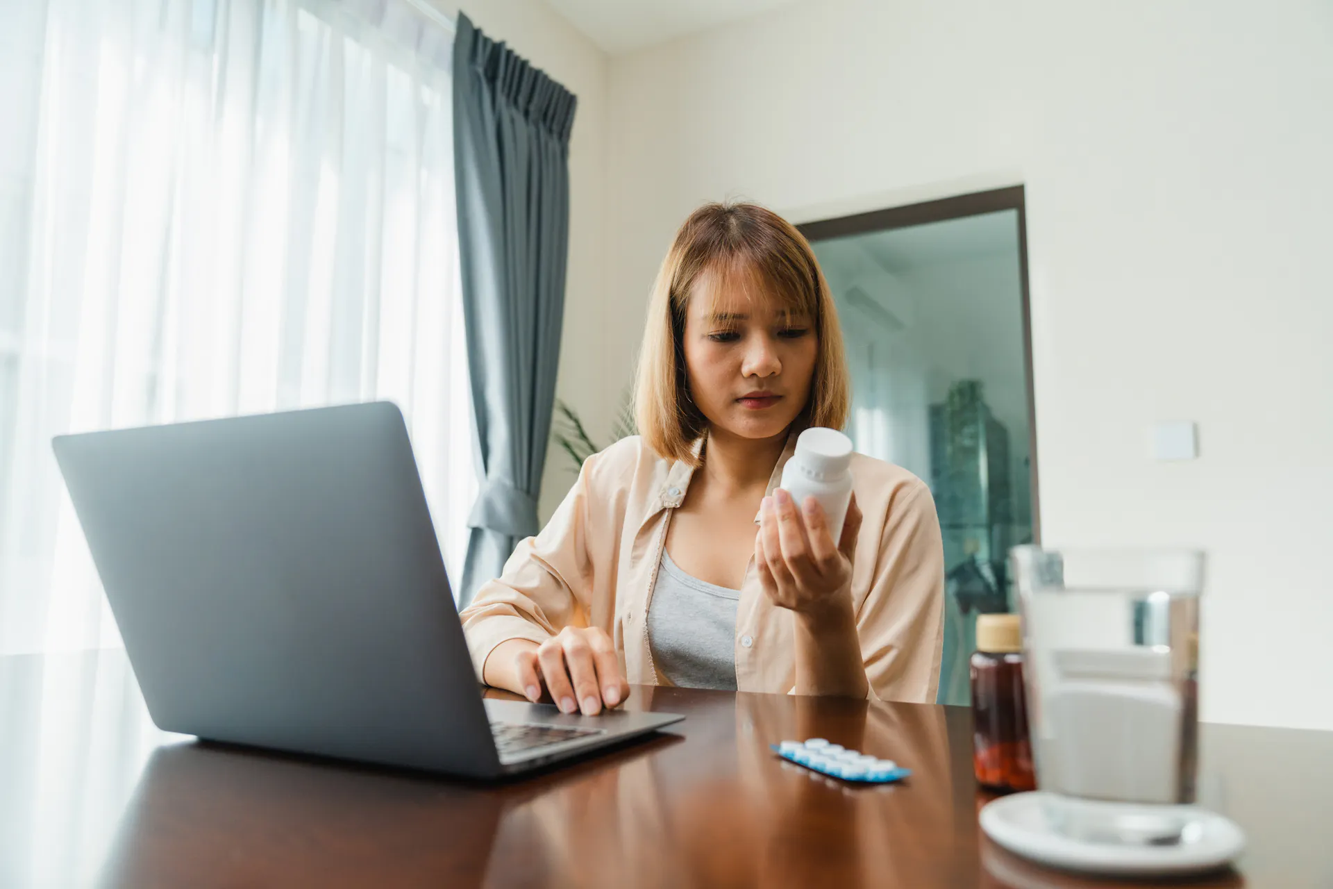 Young woman hold medicine searching information online by laptop in living room at home.