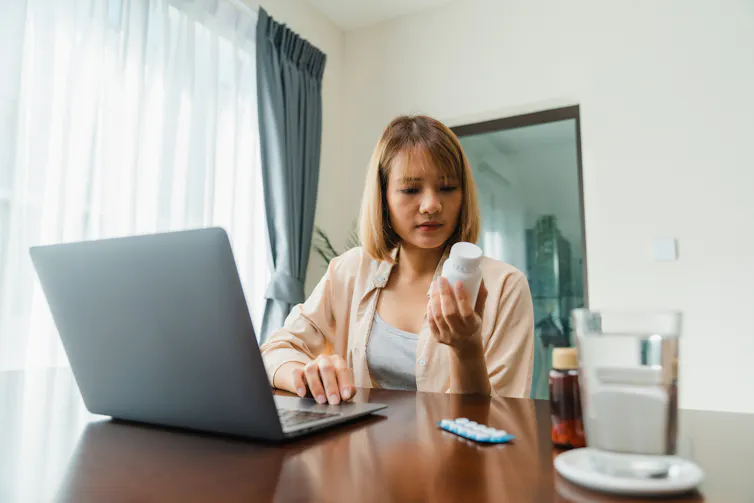 Young woman hold medicine searching information online by laptop in living room at home.
