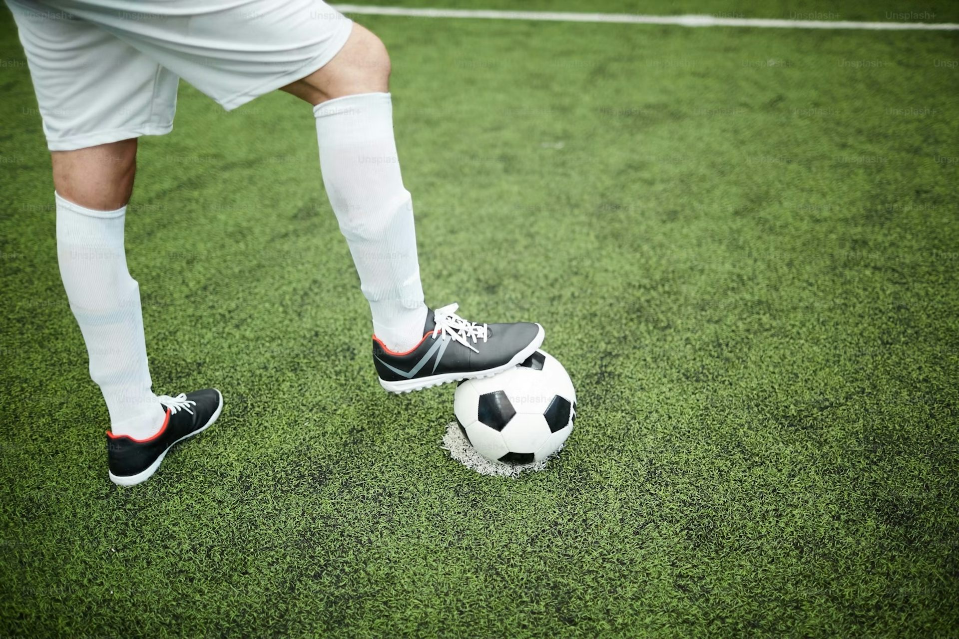 Primer plano de los pies de un jugador de fútbol mientras uno sostiene el balón de fútbol.