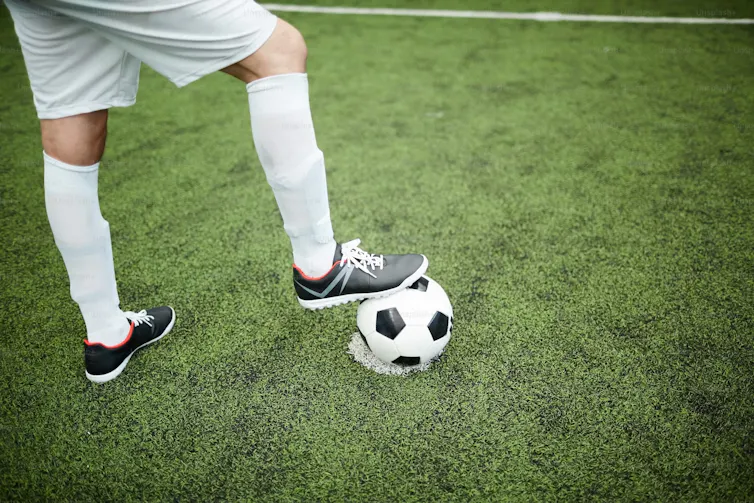 A close-up of a soccer player's feet as he props one on a soccer ball.