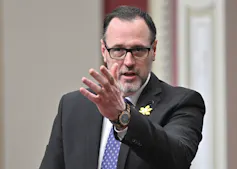 Un hombre con cabello ralo, barba y gafas hace gestos mientras habla.