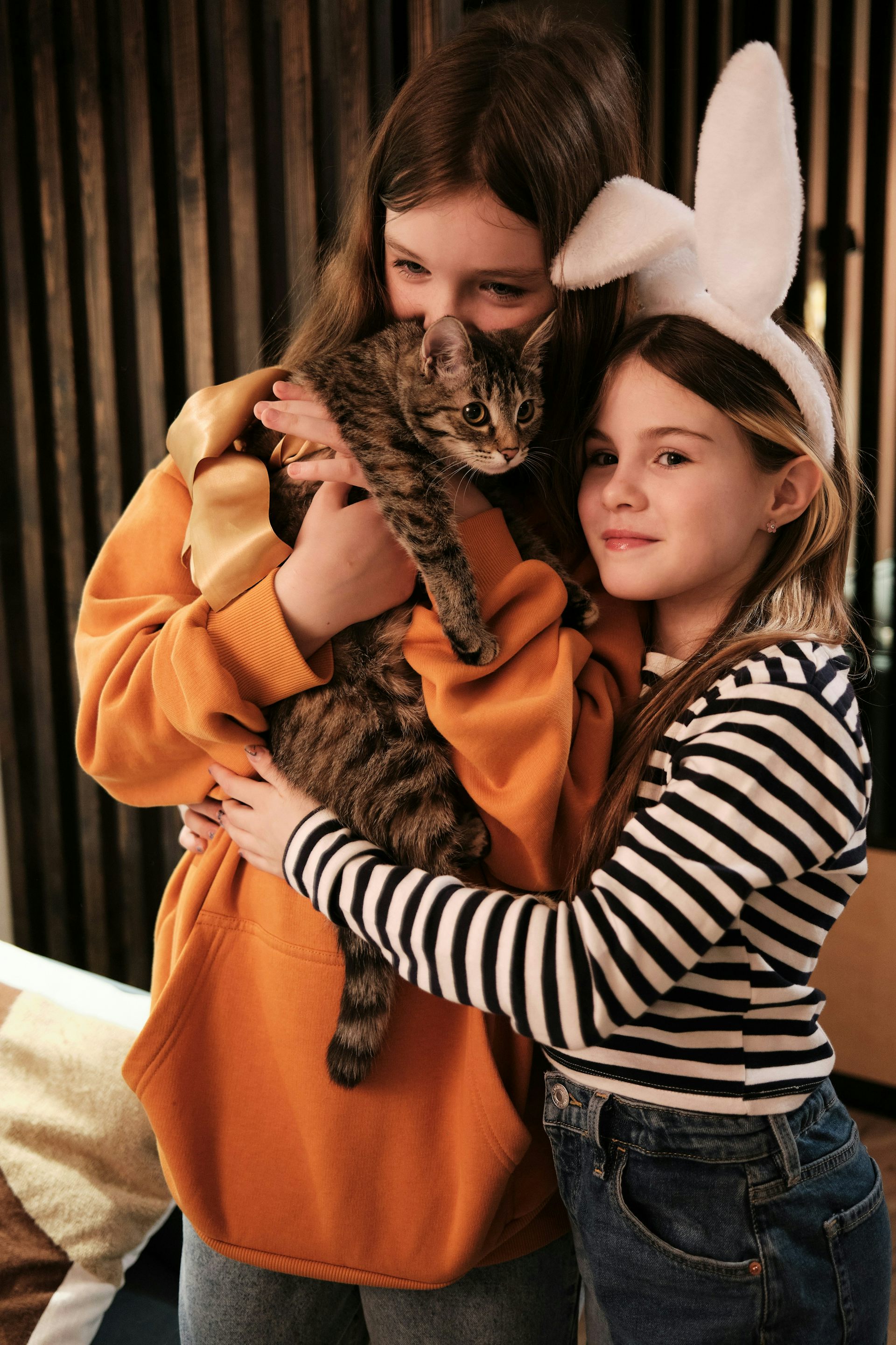 Dos niñas se abrazan mientras acarician a un gato.