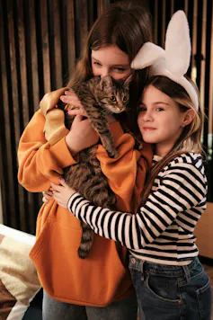 Dos niñas se abrazan mientras acarician a un gato.