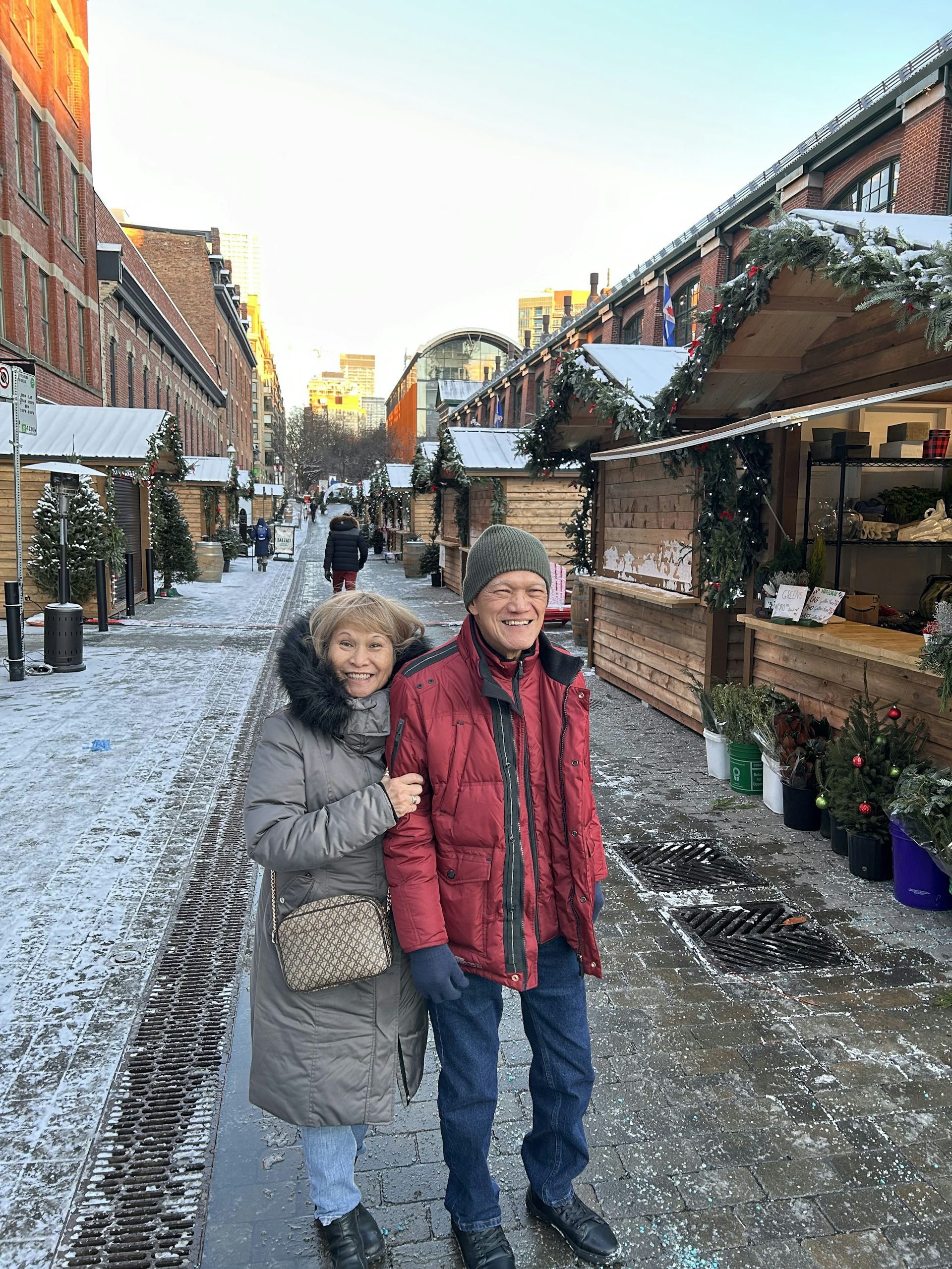 Dos adultos mayores posan sonriendo para una foto en un mercado navideño.