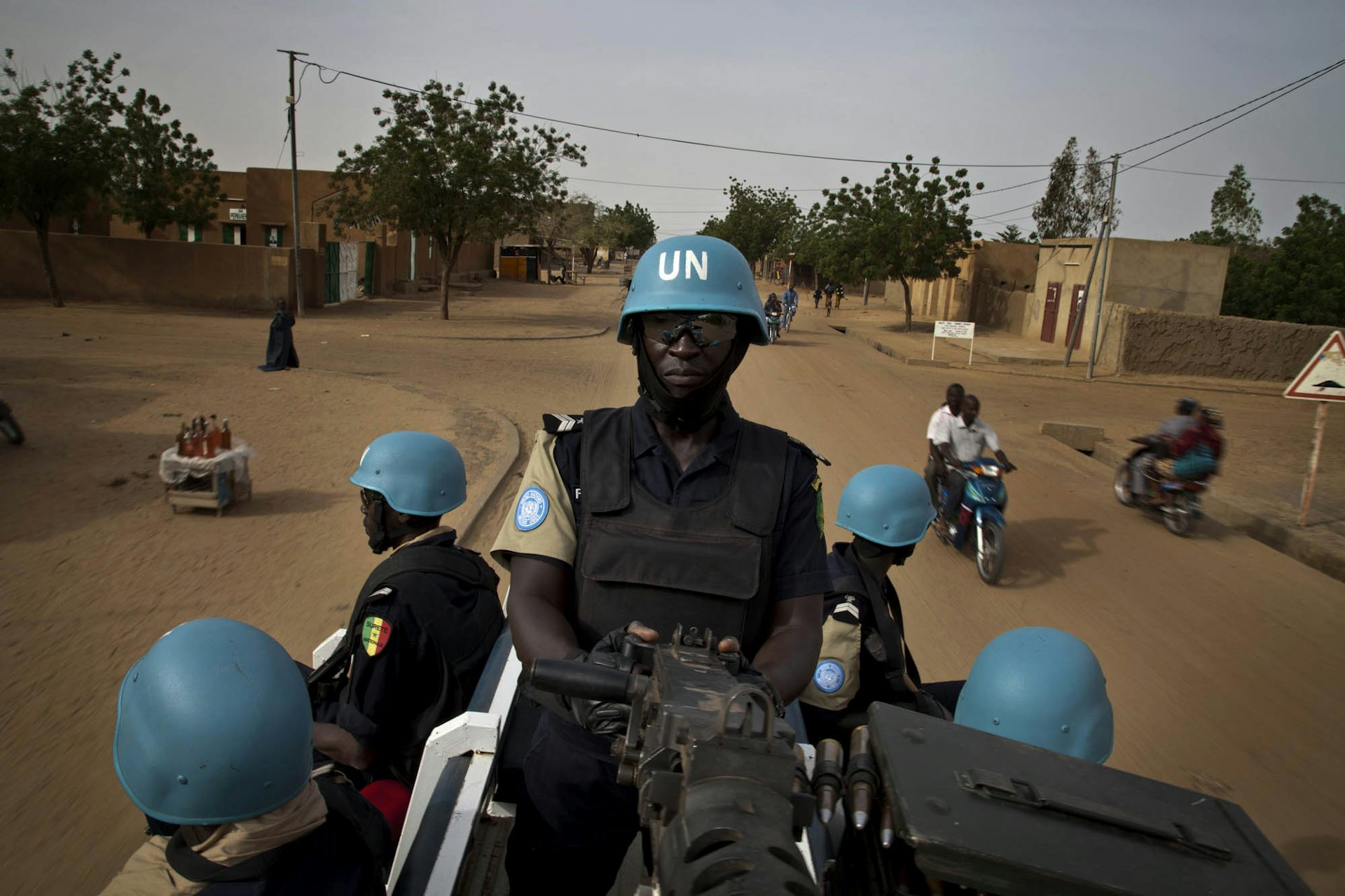 Five men wearing army fatigues and blue helmets with the letters UN in white, seated on the back of a vehicle