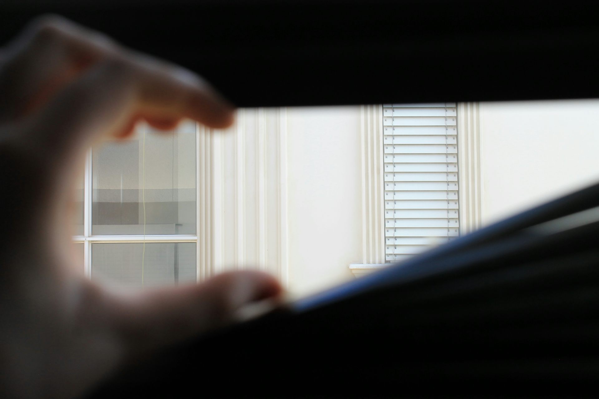 A hand opens a set of window blinds from inside.