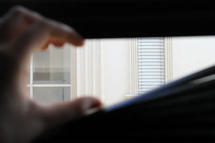 A hand opens a set of window blinds from inside.