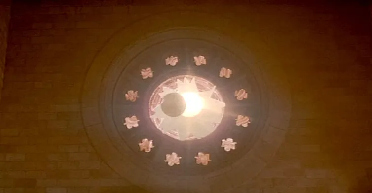 En un ventanuco en la pared se ve cómo la luna cubre parcialmente el sol.