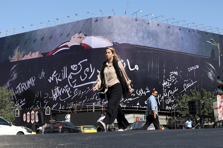 An Iranian woman walks next to a billboard in Tehran featuring Donald Trump in a coffin.