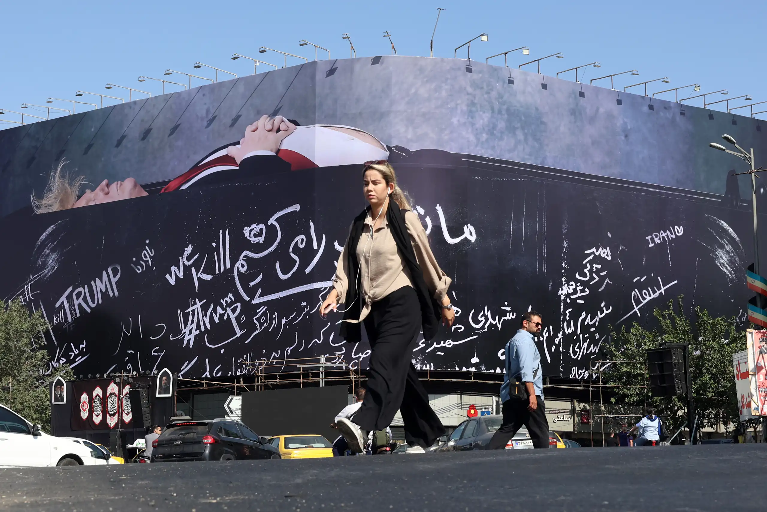 An Iranian woman walks next to a billboard in Tehran featuring Donald Trump in a coffin.