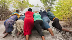 A group of people push a car out of deep mud