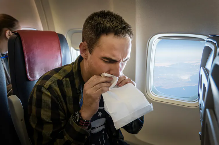 A nauseous male air passenger breathes into a bag while on a flight.