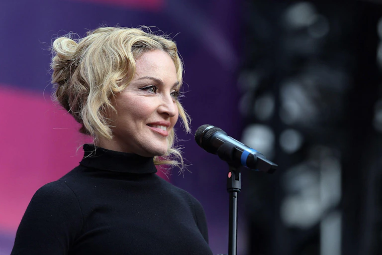 Madonna on stage at a microphone in a black polo neck.