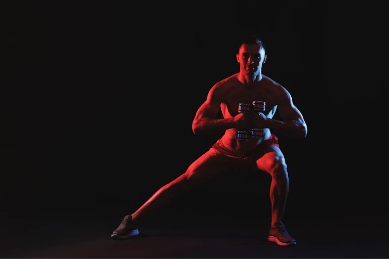 Man exercising with dumbbells in red light on black background