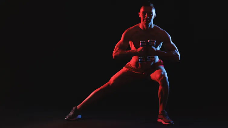 Man exercising with dumbbells in red light on black background