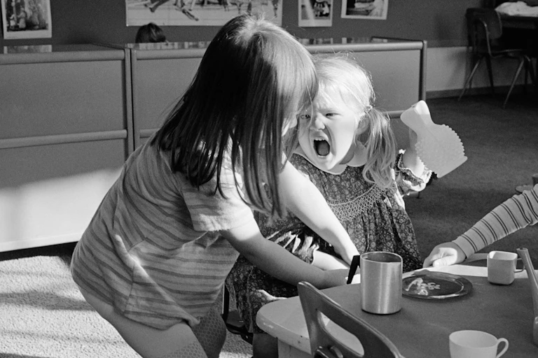 Two small children lean into each other and one cries in a black and white photo.