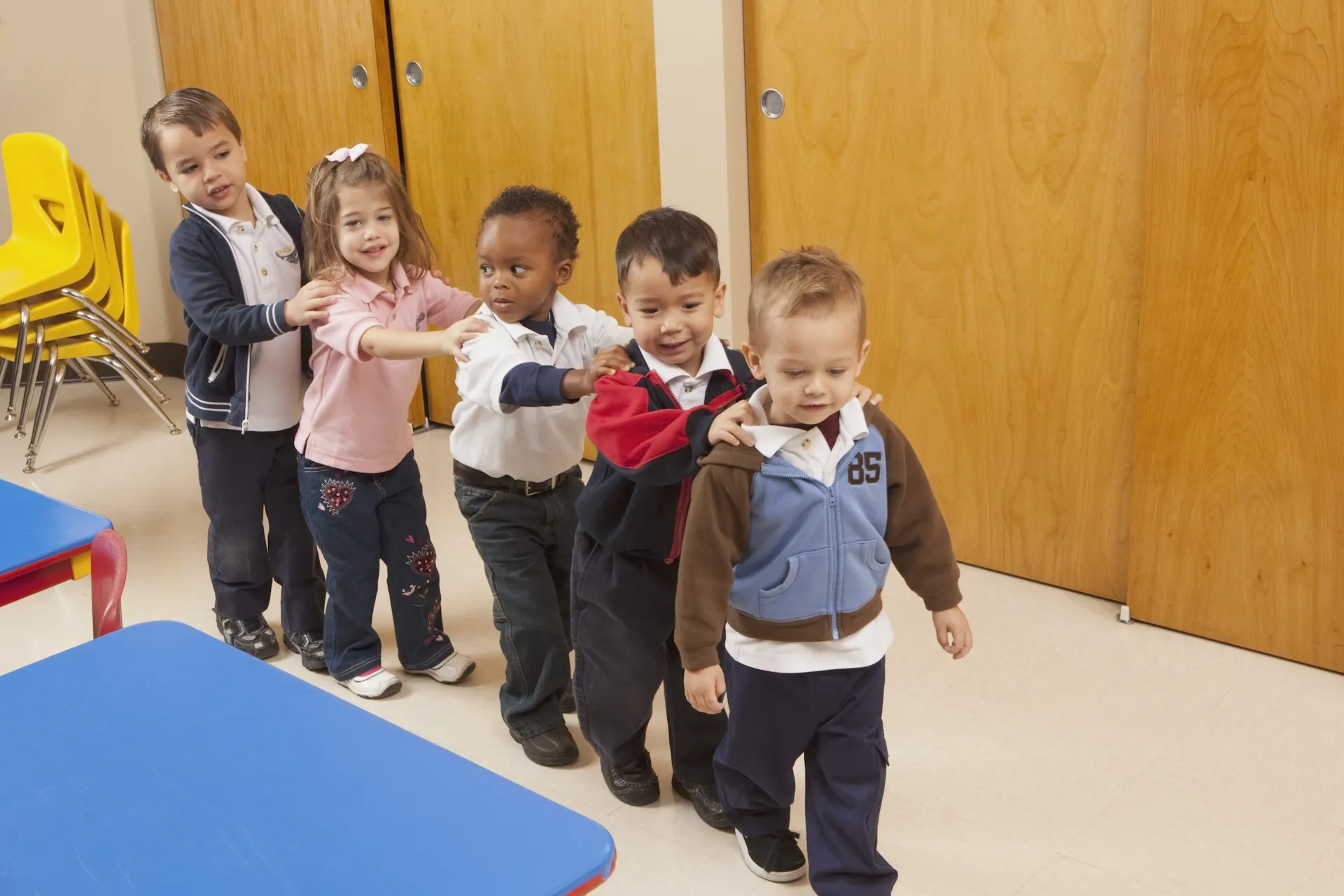 Five small children stand in a row, with their hands on their shoulders.
