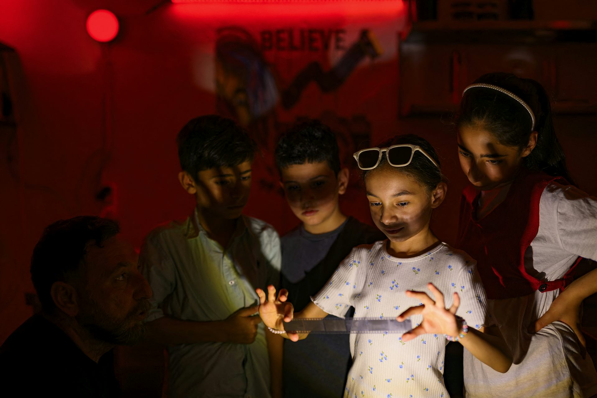 Un groupe d'enfants se rassemble autour d'une fillette qui tient une bande de pellicule développée dans une chambre noire.
