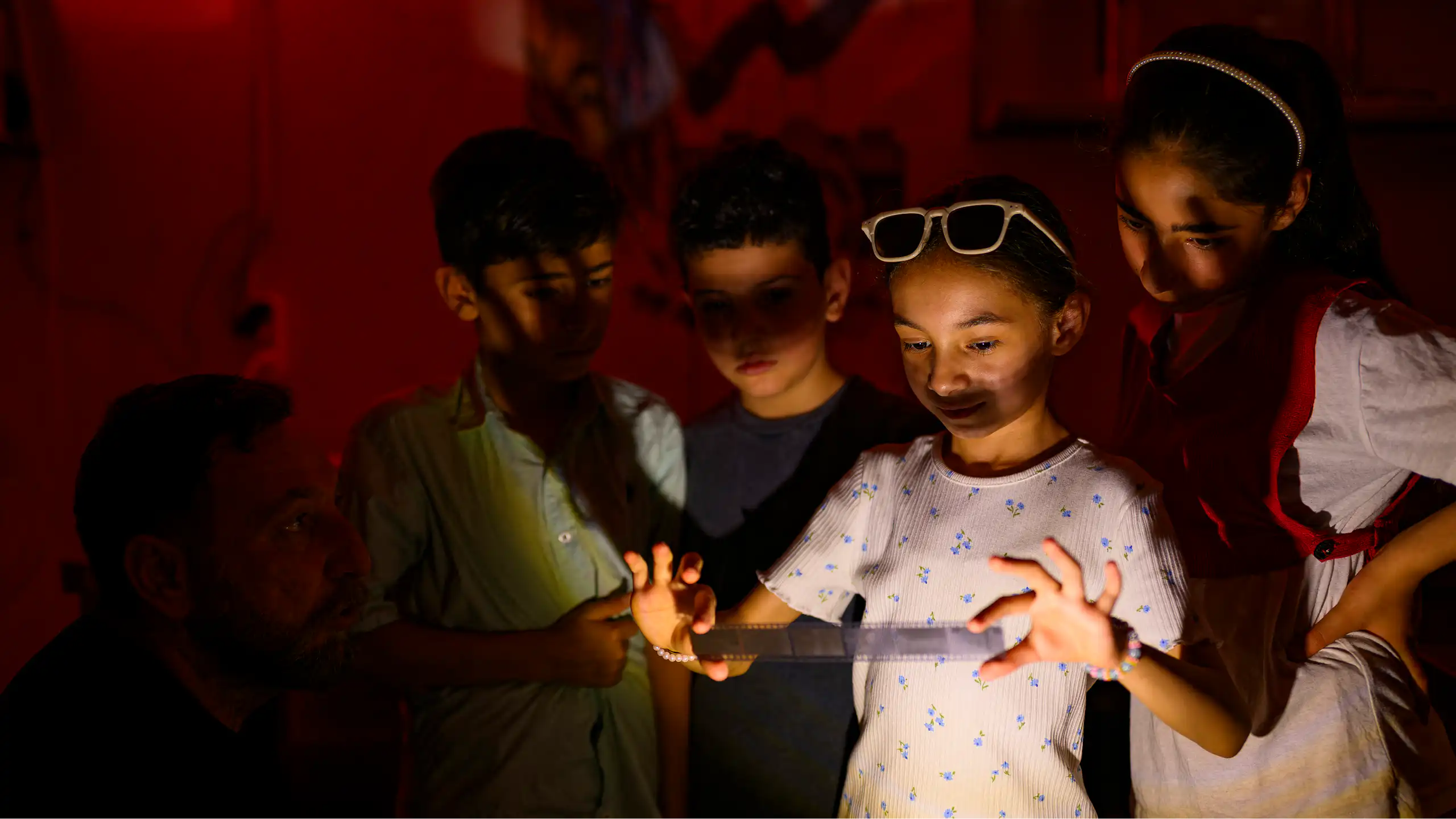 Un groupe d'enfants se rassemble autour d'une fillette qui tient une bande de pellicule développée dans une chambre noire.