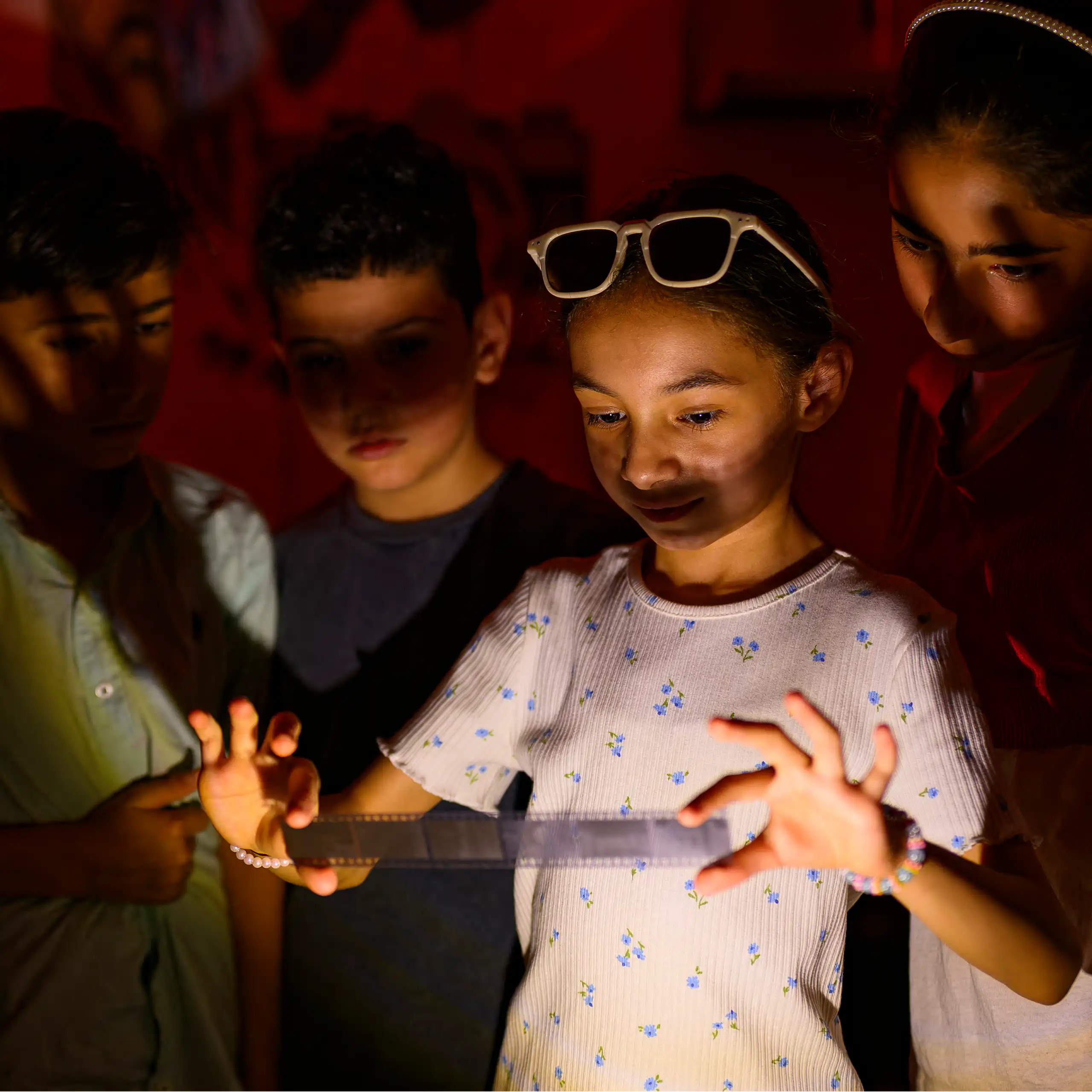 Un groupe d'enfants se rassemble autour d'une fillette qui tient une bande de pellicule développée dans une chambre noire.