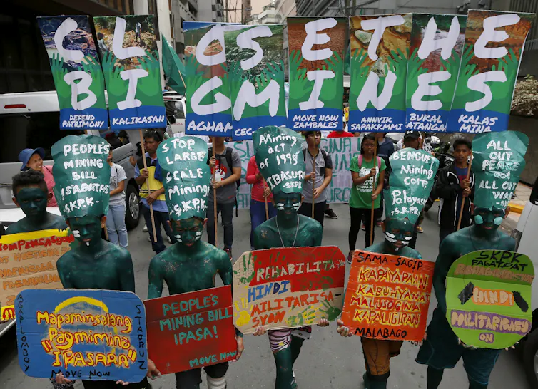 Des manifestants aux corps peints en verts brandissent des affiches colorées