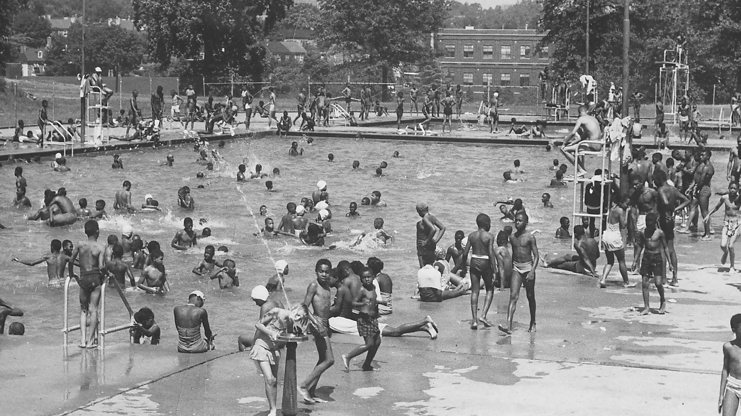 Black and white photo of dozens of Black children in a large swimming pool
