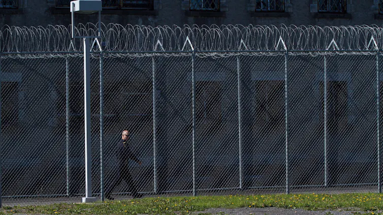 A correctional officer walks inside the fence of a penitentiary