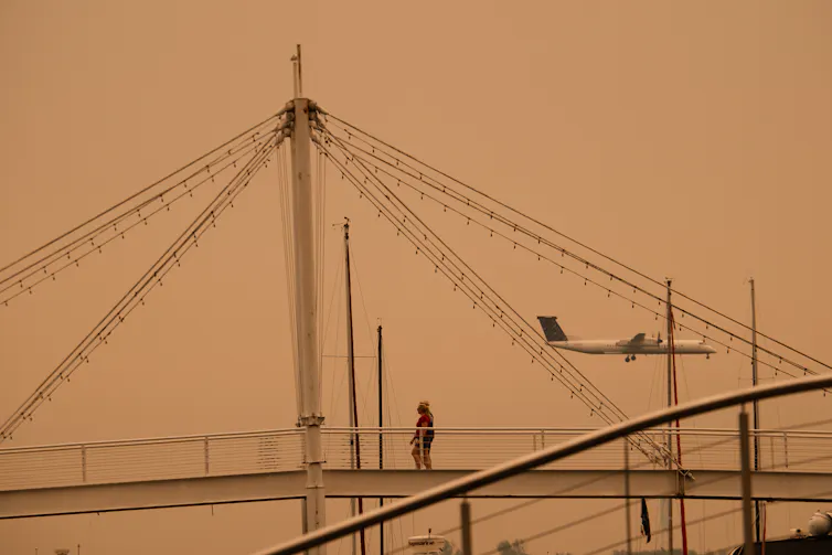 Avión en neblina naranja visto a través de soportes de puentes.
