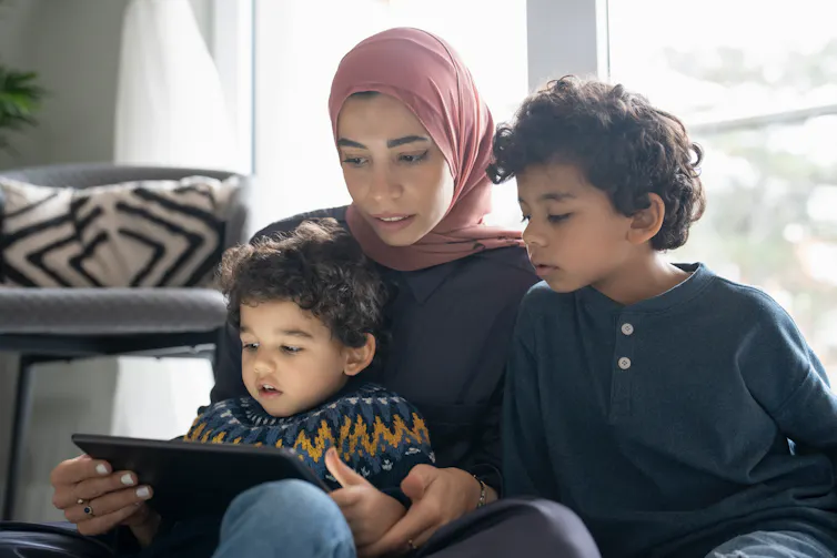 A woman and two small children look at tablet screen