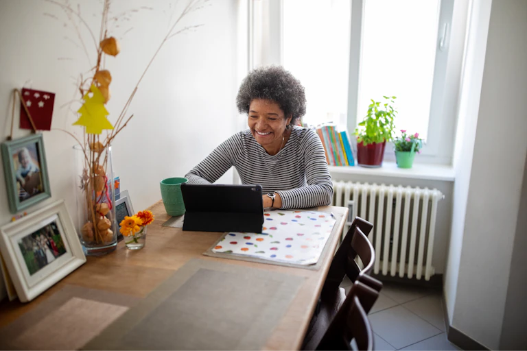 Person at home, sitting at the dining table, having a video call with on a tablet.