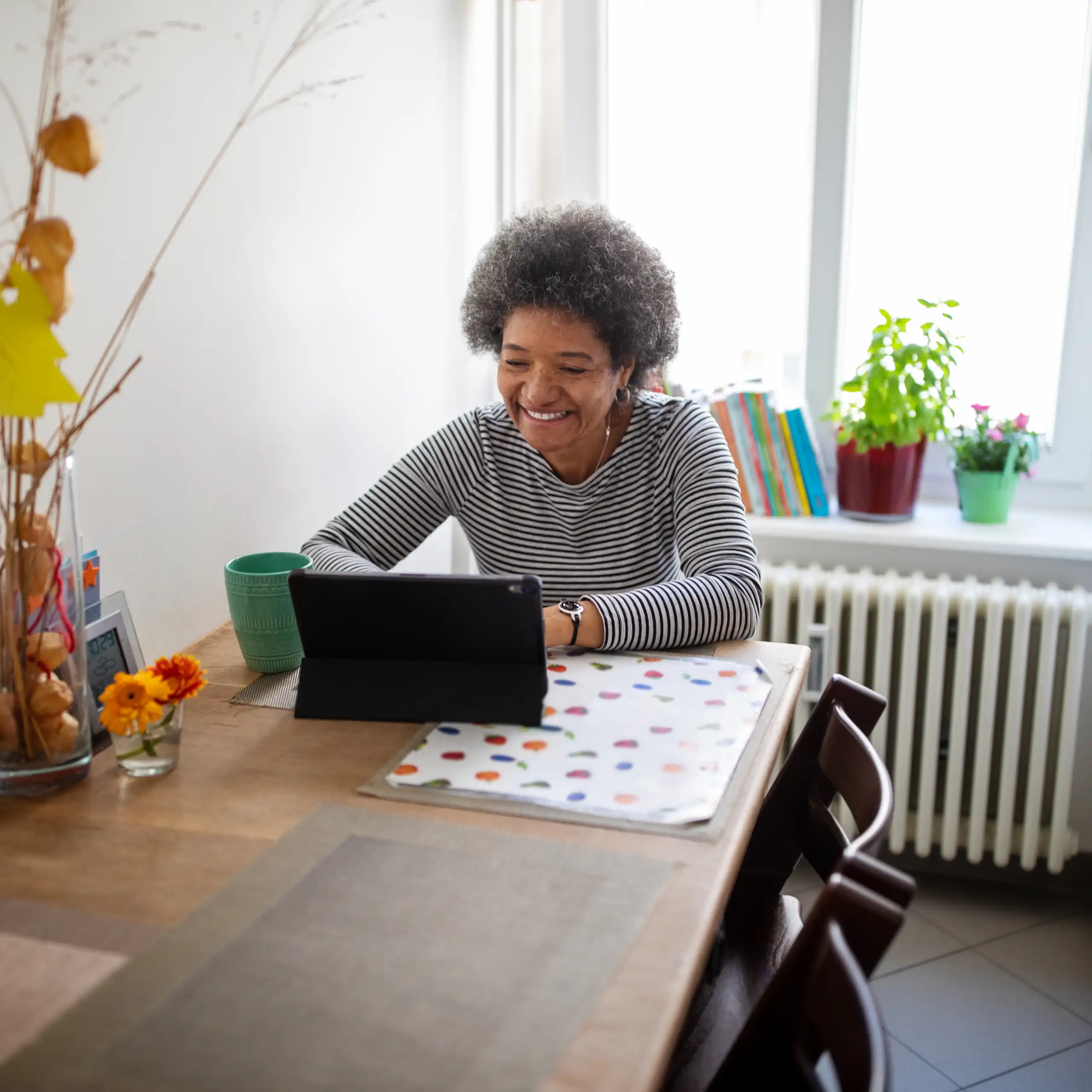 Person at home, sitting at the dining table, having a video call with on a tablet.